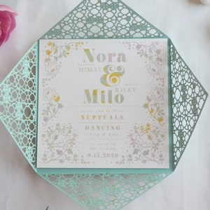 May include: A light blue and white wedding invitation with a floral design and gold lettering. The invitation reads "Nora Himat & Milo Riley" and includes the date "8.16.2020".