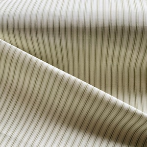May include: Close-up of a fabric with a cream background and vertical olive green stripes. The fabric is folded, showing the texture and pattern. Suitable for home decor or sewing projects.