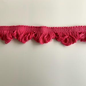 May include: Pink ruffled trim with a scalloped edge. This trim is made of a soft, woven fabric and is perfect for adding a touch of elegance to any project.