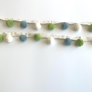 Puede incluir: Dos filas de ribete de pompón en blanco, verde, azul y blanco. Los pompones están sujetos a una cinta de color crema. El ribete es ideal para añadir un toque decorativo a diversos proyectos de manualidades, como ropa, accesorios o decoración del hogar.