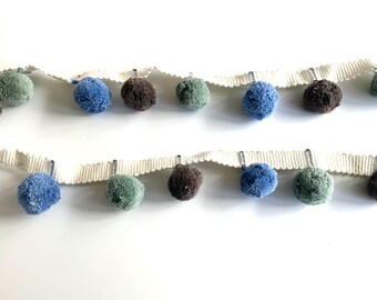 May include: A white trim with blue, green, and brown pom-poms. The trim is perfect for adding a touch of whimsy to any project.