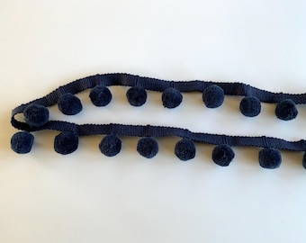 May include: A navy blue trim with pom poms. The trim is made of a soft, fuzzy material and has a row of pom poms on each side.