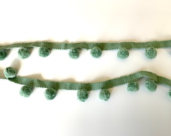 May include: A green pom-pom trim with a row of fluffy pom-poms on a green ribbon.
