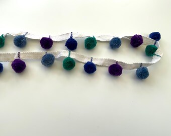 May include: A white trim with blue, purple, and green pom poms.