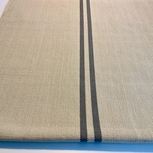 May include: A rectangular beige linen table runner with two vertical charcoal gray stripes running down the center. The fabric has a textured appearance, and the runner is displayed on a white surface.
