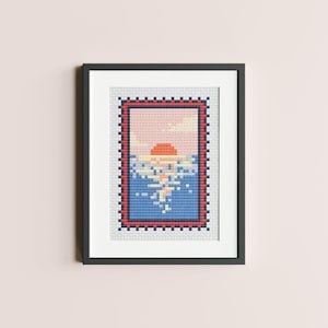 May include: A framed cross-stitch design featuring a sunset over a blue ocean. The design is surrounded by a red and blue border.