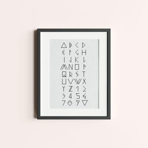 May include: A black framed print with a white background and a geometric alphabet design. The letters are made up of triangles and lines.