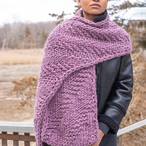 May include: A mauve knitted scarf with a textured pattern. The scarf is draped around the neck of a person wearing a black leather jacket.