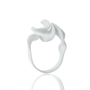 May include: A white, abstract, 3D printed ring with a unique, organic design. The ring is smooth and has a flowing, wave-like shape.