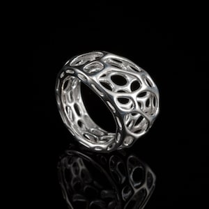 Puede incluir: Un anillo de plata con un diseño geométrico calado. El anillo está hecho de un patrón delicado e intrincado de círculos y líneas interconectados.