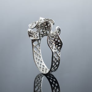 May include: A silver ring with a unique, intricate, and organic design. The ring is made of a delicate, openwork pattern that resembles a flower or a piece of coral.