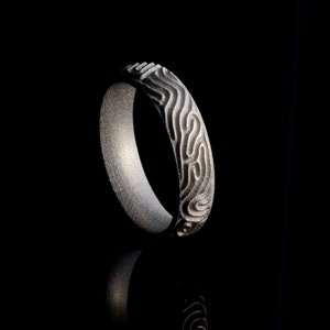 May include: A silver ring with a textured, wavy design. The ring is made of metal and has a polished finish.