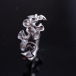 May include: A silver ring with a unique, organic design resembling a cluster of wavy, interconnected leaves.