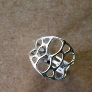 Puede incluir: Un anillo de plata con un diseño geométrico que presenta una serie de círculos interconectados.