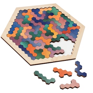 Puede incluir: Rompecabezas de madera con marco hexagonal y piezas entrelazadas de colores. El rompecabezas está parcialmente ensamblado, revelando un espacio blanco. Varias piezas sueltas en tonos naranja, verde, azul y rosa están dispersas cerca. Un juguete divertido y educativo.