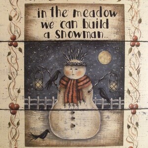 May include: A rustic wooden sign with a winter scene painted on it. The sign features a snowman with a red and white striped scarf, two black birds, and a lantern. The text on the sign reads "...in the meadow we can build a snowman..."