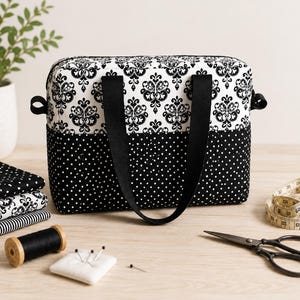 Può includere: Una borsa in tessuto rettangolare con un motivo damascato bianco e nero nella parte superiore e un tessuto nero a pois bianchi nella parte inferiore. La borsa include due manici in tessuto nero e una chiusura a zip sulla parte superiore.