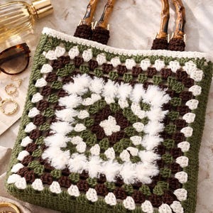 May include: A handmade crochet tote bag with a granny square design in shades of green, brown, and white. The bag features bamboo handles and a sturdy construction, perfect for carrying essentials. The bag is a stylish accessory.