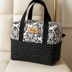 May include: A black and white patterned tote bag with black handles. The top portion features a white background with a black floral design, while the bottom has a black background with white polka dots. A small leather tag reads "Fely".