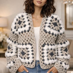 May include: A beige, white, and dark gray crochet jacket with a granny square design. The jacket has a fluffy trim on the sleeves and is worn open. The model is wearing blue jeans.