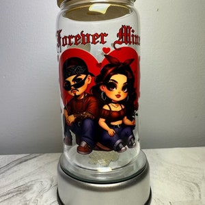 Op de afbeelding: Een glazen pot met een houten deksel en een zilveren voet. De pot heeft een afbeelding van een cartoonkoppel met de tekst "Forever Mine" erop.