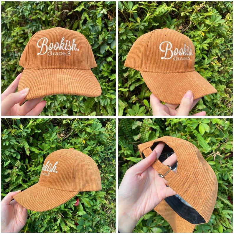 May include: A corduroy baseball cap in a warm brown color. The cap features the word "Bookish" embroidered in white script on the front. The brim is curved, and the cap has an adjustable strap.
