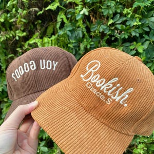 May include: Two corduroy baseball caps. One is brown with the text "sooo uoy" embroidered in white. The other is tan with the text "Bookish. Grace.S" embroidered in white. The caps have a curved brim.