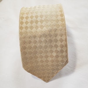 May include: A tan-colored necktie with a repeating square pattern. The tie is made of a woven fabric and has a classic pointed end. The tie is suitable for formal or business attire.