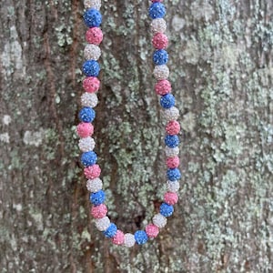 May include: A necklace made of pink, blue, and white beads. Each bead is covered in small, clear rhinestones.
