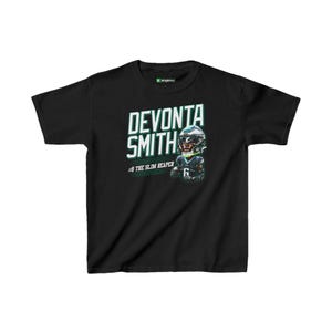 Puede incluir: Camiseta negra con un gráfico verde y blanco de un jugador de fútbol americano con casco. El texto "Devonta Smith #6 The Slim Reaper" está impreso en la camiseta.