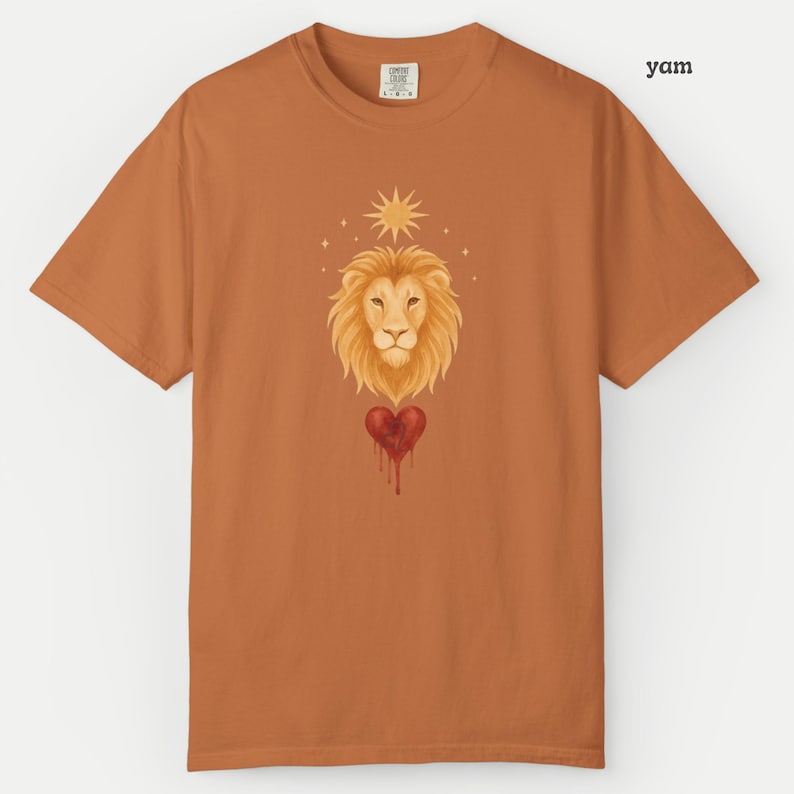 Comfort Colors Yam orange t-shirt showing a bold Leo lion illustration with a bleeding heart and glowing sun motif in warm earthy tones.