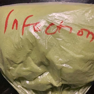 Könnte beinhalten: Ein grünes Pulver in einem durchsichtigen Plastikbeutel mit dem Wort "Infusion" in Rot.