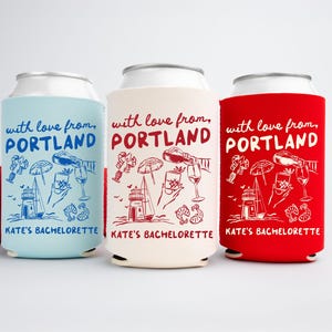 May include: Three beverage can coolers in light blue, cream, and red, each with a white graphic and text. The text reads "with love from, PORTLAND" and "KATE'S BACHELORETTE". The graphics include a lighthouse, sailboat, and wine glasses.