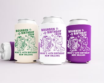 May include: Three beverage can coolers in cream, white, and purple, each with a different design. The design features two cartoon alligators playing musical instruments, with text that reads "Bourbon Birthday Crew" and "Mike's 40th Birthday New Orleans."