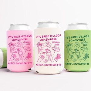May include: Three can coolers in pink, cream, and green, with the text "IT'S BRIDE O'CLOCK SOMEWHERE October 2026" and "KATIE'S BACHELORETTE". Each cooler features a beach-themed graphic with palm trees, waves, and cocktails.
