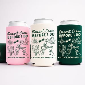 May include: Three can coolers in pink, cream, and dark green, each with a white graphic and the text "Desert Crew Before I Do" and "Caitlin's Bachelorette." The design includes cacti, sunglasses, and cocktails. One cooler is lying on its side.