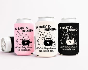 Puede incluir: Tres enfriadores de latas de espuma en rosa, blanco y negro, cada uno con un fantasma revolviendo un caldero con el texto A BABY IS BREWING, Kate's Baby Shower y DUE OCTOBER 2026. Un pequeño icono de biberón está impreso junto al caldero.