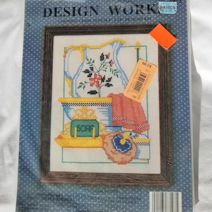 May include: A counted cross stitch kit featuring a colorful illustration of a pitcher, soap, and other bathroom items. The kit includes 100% cotton Aida cloth, embroidery floss, needle, and illustrated instructions. The kit is titled "Powder Room" and is from Design Works Crafts, Inc.
