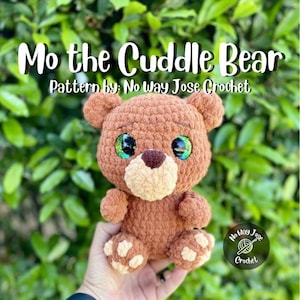 May include: A crocheted brown teddy bear with large, colorful eyes and a cream-colored muzzle. The bear is labeled "Mo the Cuddle Bear" and "Pattern by: No Way Jose Crochet."