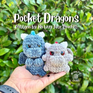 May include: Two small crochet dragon plushies, one dark blue with blue eyes and one light gray with red eyes, featuring white horns and wings. The text Pocket Dragons Pattern by: No Way Jose Crochet is displayed above the plushies.