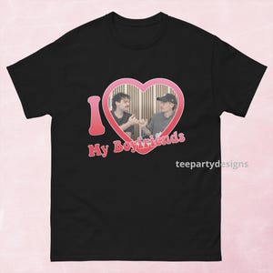Könnte beinhalten: Schwarzes T-Shirt mit einem rosa Herz, das zwei Männer enthält, und den Worten "I My Boyfriends" in Rosa. Das Design enthält den Text "teepartydesigns" in Weiß. Das T-Shirt ist aus einem weichen Material.