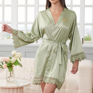Può includere: Accappatoio in raso verde salvia con finiture in pizzo sulle maniche e sull'orlo. L'accappatoio ha una cintura abbinata e un monogramma dorato sul petto. Parte della collezione "Tahi Precious Gifts".