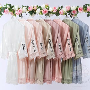 May include: A selection of satin robes in shades like white, pink, and blue, displayed on a gold rack. Each robe features lace detailing and a matching belt. The sleeves are labelled with colour names such as "White" and "Dusty Blue".