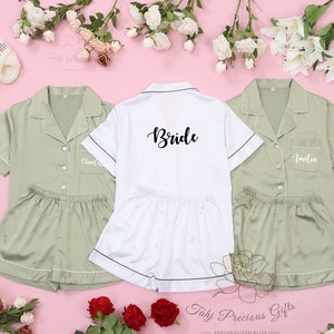 May include: Three matching satin pajamas with short sleeves and shorts. One set is white with black trim and says "Bride" on the front. The other two sets are sage green with white trim and say "Kristen" and "Amelia" on the front.
