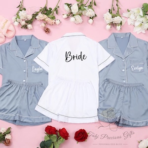 Puede incluir: Tres conjuntos de pijamas a juego en color azul claro con ribetes blancos. El pijama de la novia tiene la palabra "Bride" bordada en la parte delantera. Los otros dos conjuntos tienen los nombres "Layla" y "Evelyn" bordados en la parte delantera.