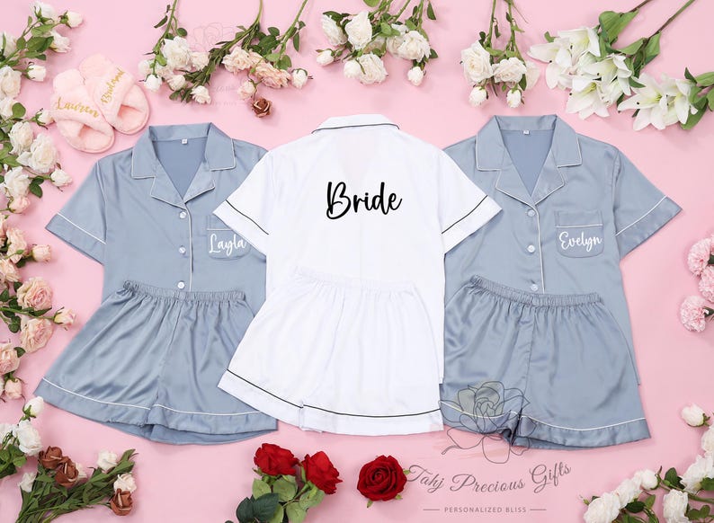 Puede incluir: Tres conjuntos de pijamas a juego en color azul claro con ribetes blancos. El pijama de la novia tiene la palabra "Bride" bordada en la parte delantera. Los otros dos conjuntos tienen los nombres "Layla" y "Evelyn" bordados en la parte delantera.