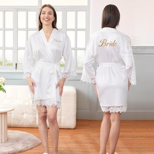 May include: White satin robe with lace trim on the sleeves and hem. The robe has a matching belt and the name "Claudia" embroidered on the front. The word "Bride" is embroidered on the back of another robe.