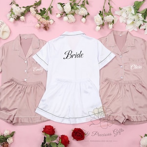 May include: Three matching satin pyjama sets in pink and white. The white set has "Bride" embroidered on the back. The pink sets have "Emily" and "Olivia" embroidered on the front.