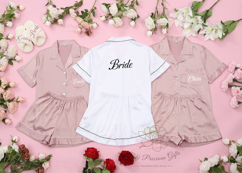 May include: Three matching satin pyjama sets in pink and white. The white set has "Bride" embroidered on the back. The pink sets have "Emily" and "Olivia" embroidered on the front.