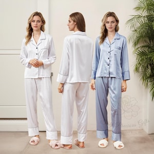 May include: Three women wearing matching pajamas in white, light blue, and dark blue. The pajamas have a collared shirt with a button-up front and long sleeves. The pants are long and have a straight leg.